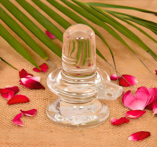 Sphatik Shivling for home pooja, 4-inch crystal showpiece with white finish, surrounded by rose petals and palm leaves.